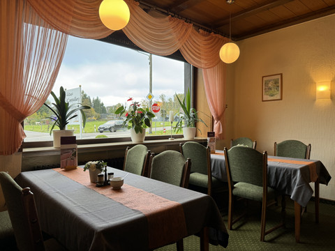 Innenansicht Restaurant - Haus Koppelberg Gemütliches Restaurantinterieur mit Holztäfelung, großen Fenstern, Pflanzen und gedeckten Tischen.