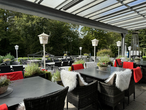 Außenterrasse - Ansicht Tropfsteinhöhle Gemütliche Terrasse eines Cafés mit überdachten Sitzbereichen, umgeben von grünen Bäumen.