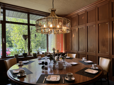 Innenansicht Waldhotel Tropfsteinhöhle Elegant gedeckter Tisch in rustikalem Raum mit Holzwänden, großer Fensterfront und Kronleuchter.