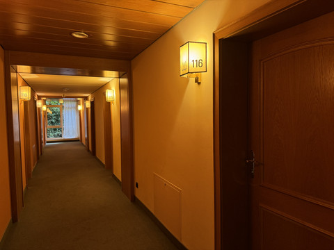 Innenansicht Flur - Waldhotel Tropfsteinhöhle Beleuchteter Hotelflur mit Türen, warmen Holztönen und einem Fenster am Ende des Ganges.