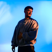 900007530_22700_pr_montez_15896.jpg Ein junger Mann in einem weiten grauen Pullover blickt nach links vor einem blauen Hintergrund.