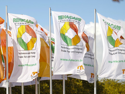 Rehacare24_MK6991.jpg Mehrere Rehacare-Banner wehen im Wind, im Hintergrund ist ein blauer Himmel.