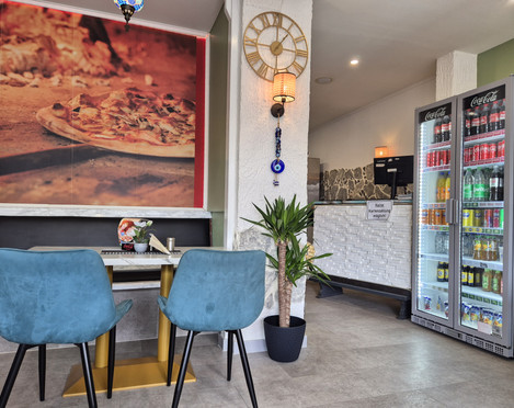 Innenansicht Pizzaria La Rosa Innenansicht einer modernen Gaststätte mit blau gepolsterten Stühlen an einem Tisch und einem Kühlschrank mit Getränken.