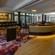 Innenraum im Restaurant merk.Mahl Moderne Hotelbar mit elegant geschwungenem Tresen, gemütlichen Ledersitzen und stimmungsvoller Beleuchtung.