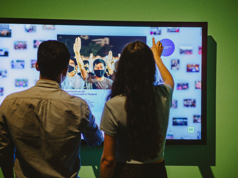Freiheit 5_Isabel Noack.jpg Zwei Personen interagieren mit einem großen, wandmontierten Touchscreen in einem Ausstellungsraum.Two people interact with a large, wall-mounted touchscreen in a showroom.Dvě osoby komunikují s velkou dotykovou obrazovkou na stěně v showroomu.Dwie osoby wchodzą w interakcję z dużym, zamontowanym na ścianie ekranem dotykowym w salonie wystawowym.Twee mensen werken met een groot aanraakscherm aan de muur in een showroom.Due persone interagiscono con un grande touchscreen montato a parete in uno showroom.