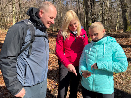 Wandern in der Mittelweser-Region Drei Wanderer in bunter Outdoor-Kleidung studieren ein Smartphone in einem lichten Wald im Herbst.