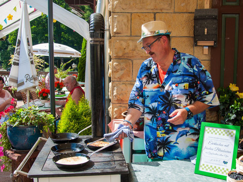 Ein Mann in bunter Hawaii-Hemd bereitet Blaubeereierkuchen auf einem Ofen im Freien zu.