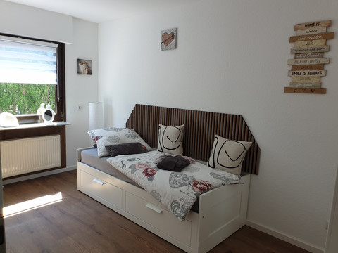 Schlafzimmer Helles Schlafzimmer mit Einzelbett, stilvoller Dekoration und großem Fenster für natürlichen Lichteinfall.