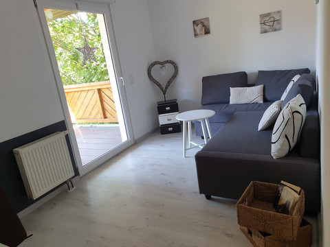 Schlafzimmer Gemütliches Wohnzimmer mit grauem Ecksofa, weißen Kissen, rundem Tisch und Zugang zu einem Balkon.