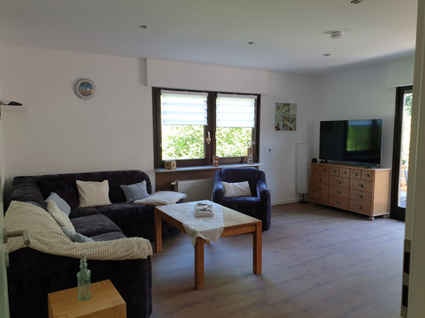 Wohnzimmer Gemütliches Wohnzimmer mit L-förmigem Sofa, Sessel, Holztisch, Flachbildfernseher und Blick ins Grüne.