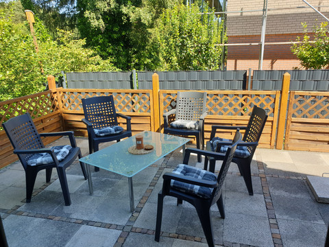 Terrasse Terrasse mit sechs schwarzen Gartenstühlen um einen Glastisch, umgeben von Holzsichtschutz und Pflanzen.