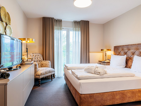 Victor's Residenz - Hotel Gummersbach Gemütliches Hotelzimmer mit Doppelbett, elegant dekoriert, Sessel, Flachbildfernseher und Fensterblick.