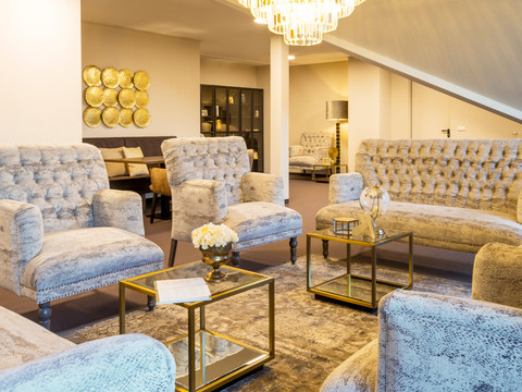 Victor’s Residenz-Hotel Gummersbach Gemütlicher Loungebereich mit eleganten, gepolsterten Sitzmöbeln und stilvollen goldenen Akzenten.