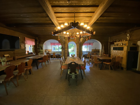 Holzverkleideter Speiseraum mit langen Tischen und stimmungsvoller Beleuchtung unter einem Balkendecke.