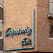 Chlodwig Eck Neonschriftzug "Chlodwig Eck" an einem Backsteingebäude, leicht verwittert, darunter das Eingangsschild.Neon lettering "Chlodwig Eck" on a brick building, slightly weathered, with the entrance sign underneath.