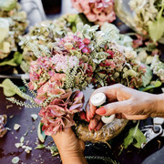 Greenshot 2025-07-14 11.39.02.png Eine Person arrangiert bunte Hortensienblüten zu einem Strauß und besprüht diese sorgfältig.