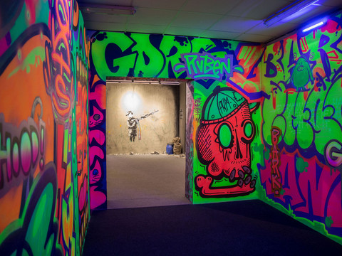 Neonfarbene Wände mit Graffiti und im Hintergrund ein Banksy-Wandgemälde eines Mädchens.Neon-colored walls with graffiti and a Banksy mural of a girl in the background.Neonové zdi s graffiti a Banksyho nástěnnou malbou dívky v pozadí.Neonowe ściany z graffiti i muralem Banksy'ego przedstawiającym dziewczynę w tle.Neonkleurige muren met graffiti en een Banksy muurschildering van een meisje op de achtergrond.Pareti colorate al neon con graffiti e un murale di Banksy raffigurante una ragazza sullo sfondo.