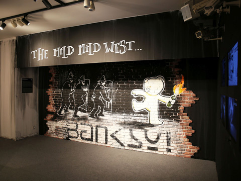 Graffiti von Banksy in einer Leipziger Galerie, zeigt Polizisten und ein strahlendes Kind.Graffiti by Banksy in a Leipzig gallery, showing police officers and a beaming child.Banksyho graffiti v lipské galerii, na kterém jsou zobrazeni policisté a rozzářené dítě.Graffiti autorstwa Banksy'ego w galerii w Lipsku, przedstawiające policjantów i uśmiechnięte dziecko.Graffiti van Banksy in een galerie in Leipzig, met politieagenten en een stralend kind.Graffiti di Banksy in una galleria di Lipsia, raffiguranti agenti di polizia e un bambino raggiante.