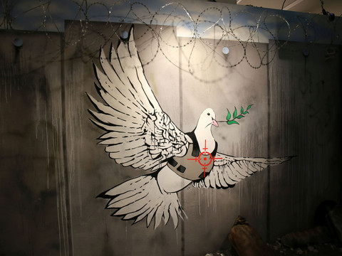 10 House of Banksy - Leipzig - Foto Andreas Schmidt.jpg Ein Graffiti zeigt eine fliegende Taube in einer kugelsicheren Weste mit einem Ölzweig im Schnabel.One graffiti shows a flying pigeon in a bulletproof vest with an olive branch in its beak.Na jednom graffiti je zobrazen letící holub v neprůstřelné vestě s olivovou ratolestí v zobáku.Jedno z graffiti przedstawia latającego gołębia w kamizelce kuloodpornej z gałązką oliwną w dziobie.Eén graffiti toont een vliegende duif in een kogelvrij vest met een olijftak in zijn snavel.Un graffito mostra un piccione volante con un giubbotto antiproiettile e un ramo d'ulivo nel becco.