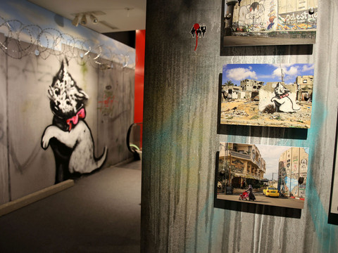 Museumsraum mit Banksy-Street-Art, darunter Katzengraffiti und Fotografien zerstörter Gebäude.Museum room with Banksy street art, including cat graffiti and photographs of destroyed buildings.Muzejní místnost s Banksyho pouličním uměním, včetně kočičích graffiti a fotografií zničených budov.Pokój muzealny ze sztuką uliczną Banksy'ego, w tym kocie graffiti i zdjęcia zniszczonych budynków.Museumzaal met straatkunst van Banksy, waaronder kattengraffiti en foto's van verwoeste gebouwen.Sala del museo con la street art di Banksy, tra cui graffiti di gatti e fotografie di edifici distrutti.