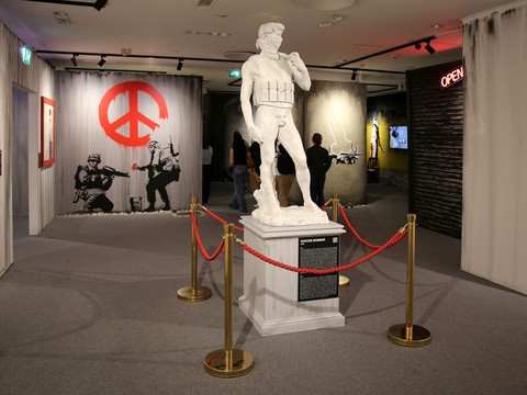 8 House of Banksy - Leipzig - Foto Andreas Schmidt.jpg Eine Statue im Banksy-Stil im Vordergrund, umgeben von politischer Straßenkunst.A Banksy-style statue in the foreground, surrounded by political street art.Socha ve stylu Banksyho v popředí, obklopená politickým pouličním uměním.Pomnik w stylu Banksy'ego na pierwszym planie, otoczony polityczną sztuką uliczną.Een standbeeld in Banksy-stijl op de voorgrond, omringd door politieke straatkunst.Una statua in stile Banksy in primo piano, circondata da street art politica.