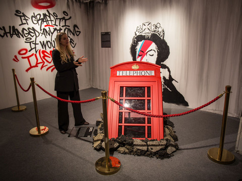 3 House of Banksy - Leipzig - Foto Andreas Schmidt.jpg Kunstinstallation mit roter Telefonzelle und Graffiti von Banksy, inklusive Queen-Motiv in Ausstellung.Art installation with red telephone box and graffiti by Banksy, including Queen motif on display.Umělecká instalace s červenou telefonní budkou a graffiti od Banksyho, včetně motivu královny.Instalacja artystyczna z czerwoną budką telefoniczną i graffiti autorstwa Banksy'ego, w tym motyw królowej.Kunstinstallatie met rode telefooncel en graffiti van Banksy, waaronder het motief van de koningin.Installazione artistica con cabina telefonica rossa e graffiti di Banksy, tra cui il motivo dei Queen.