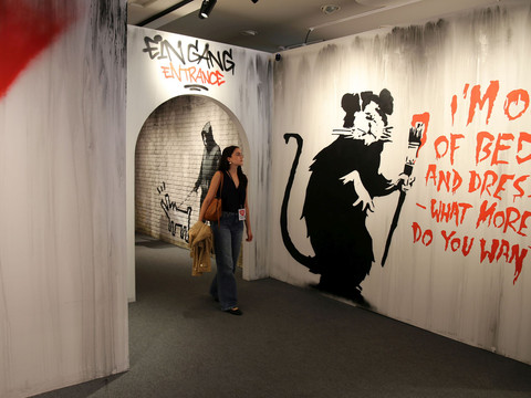 1 House of Banksy - Leipzig - Foto Andreas Schmidt.jpg Frau spaziert in Galerie mit berühmten Banksy-Graffiti und Text an weißen Wänden.Woman walks into gallery with famous Banksy graffiti and text on white walls.Žena vchází do galerie se slavnými Banksyho graffiti a texty na bílých stěnách.Kobieta wchodzi do galerii ze słynnym graffiti Banksy'ego i tekstem na białych ścianach.Vrouw loopt galerie binnen met beroemde Banksy graffiti en tekst op witte muren.Una donna entra in una galleria con i famosi graffiti e testi di Banksy su pareti bianche.