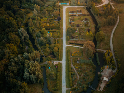 Luftaufnahme eines Parks mit symmetrischen Gärten und einem Herrenhaus im Hintergrund.