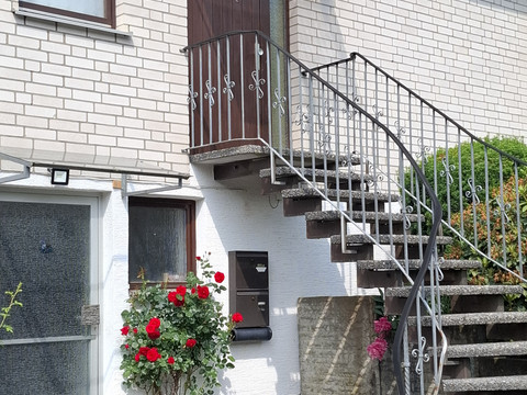Eingang FeWo 1 Außentreppe eines Hauses mit weißen Wänden, eine blühende Rosenpflanze steht daneben.