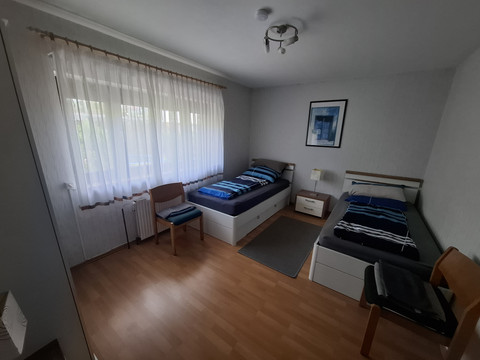 Schlafzimmer FeWo 1 Zwei Einzelbetten in einem hellen Raum mit Holzboden, ein Fenster mit weißem Vorhang.