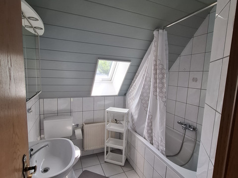 Bad FeWo 2 Badezimmer mit Duschwanne, Waschbecken und WC, Tageslicht durch ein Dachfenster erhellt den Raum.