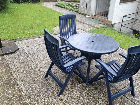 Eingang - FeWo 2 Garten mit Kiesweg, Terrasse und vier blauen Kunststoffstühlen um einen runden Tisch gruppiert.