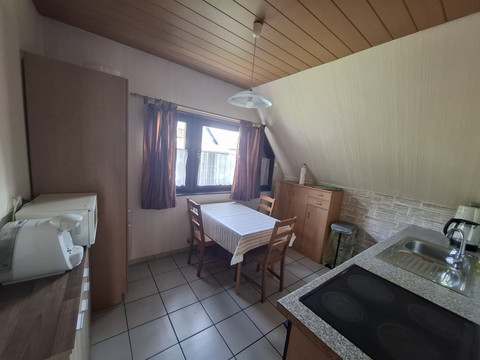 Küche FeWo 2 Gemütliche Küche mit Holzmöbeln, Tisch, vier Stühlen, Herd, Mikrowelle und großem Fenster.