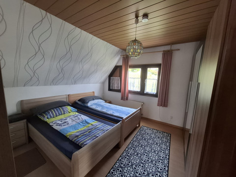 Schlafzimmer FeWo 2 Gemütliches Schlafzimmer mit zwei Einzelbetten, Holzdecke, Teppich und Fenster mit Vorhängen.