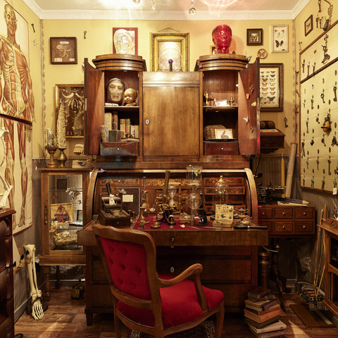 D. Zielske Wunderkammer Shooting08.jpg Ein üppig dekoriertes Arbeitszimmer mit antiken Schränken, Schädeln und wissenschaftlichen Objekten.