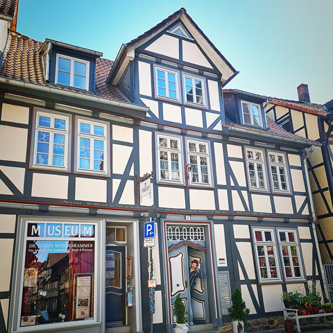 Haus Sommer25.jpg Fachwerkhaus mit weiß-blauen Fassaden, Museumsschild und Pflanzen am Eingang, blauer Himmel.