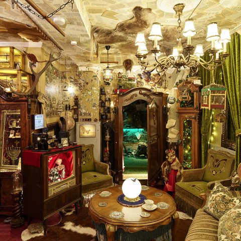 D. Zielske Wunderkammer Shooting02.jpg Ein Raum voller antiker Möbel, grüner Vorhänge, dekorativer Lampen und kunstvoller Kuriositäten.