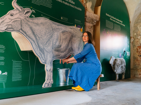 Frau in blauer Kleidung melkt Modell einer Kuh an interaktiver Ausstellungstafel.Woman in blue clothing milking a model of a cow on an interactive exhibition board.Žena v modrém oblečení dojí model krávy na interaktivní výstavní tabuli.Kobieta w niebieskim ubraniu dojąca model krowy na interaktywnej tablicy wystawowej.Vrouw in blauwe kleding melkt een model van een koe op een interactief tentoonstellingsbord.Donna vestita di blu che munge il modello di una mucca su un tabellone interattivo.