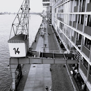 Rheinauhafen Ein Schwarz-Weiß-Foto von einer belebten Fußgängerpromenade am Wasser, flankiert von modernen Gebäuden.A black and white photo of a busy pedestrian promenade by the water, flanked by modern buildings.
