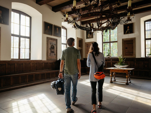 Ein Paar besichtigt ein helles, historisches Interieur mit großem Lüster und Porträts an den Wänden.