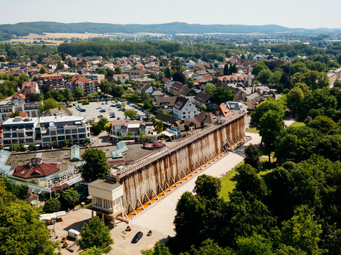 Gradierwerk in einer grünen Parklandschaft, umgeben von Stadthäusern und Hügeln im Hintergrund.