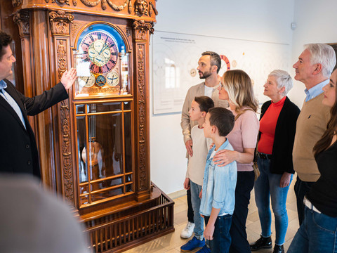Gruppe betrachtet antike Standuhr im Uhrenmuseum, geführt von einem Mann.