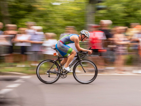 4 - Muldental Triathlon - Foto Matthias Vogel.png Ein Radfahrer in Aktion bei einem Triathlon, umgeben von applaudierendem Publikum.