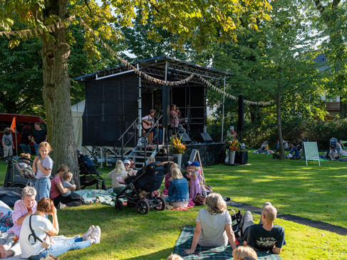 Menschen sitzen auf Picknickdecken auf einer Wiese vor einer Bühne im Freien.