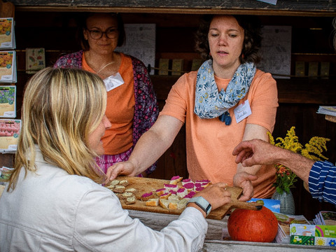 Bio-Erlebnistage 2025-c-Victor Smolinski.jpg Menschen genießen Bio-Köstlichkeiten an einem Marktstand mit freundlichem Austausch.
