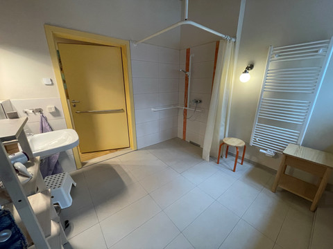 Barrierefreies, helles Badezimmer mit befahrbarer Dusche, Haltegriffen und gelber Tür mit Griff.