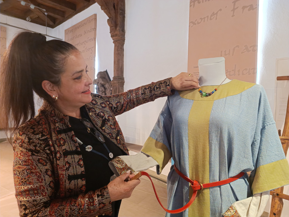 Sonntagsführungen_mit_Cristina_Lüdeke2.jpg Ein dem mittelalterlichen Gewand nachempfundenes Gewand auf einer Schneiderbüste mit einer Frau, die das Kleidungsstück erklärt