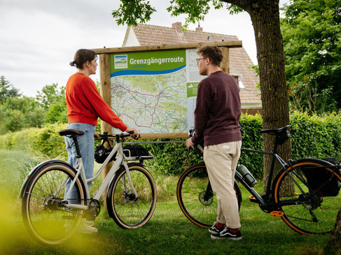 Zwei Radfahrer betrachten eine Karte der Grenzgängerrouten im Freien.
