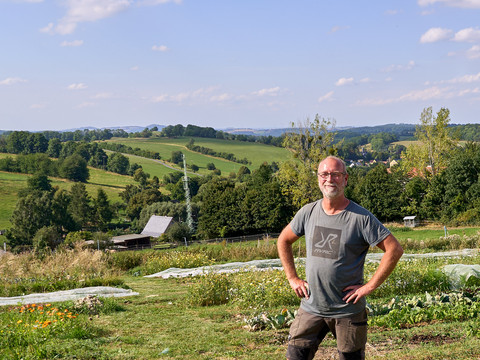 Der Eigentümer stecht mit angestellten Armen auf seinem Feld und schaut freundlich in die Kamera.