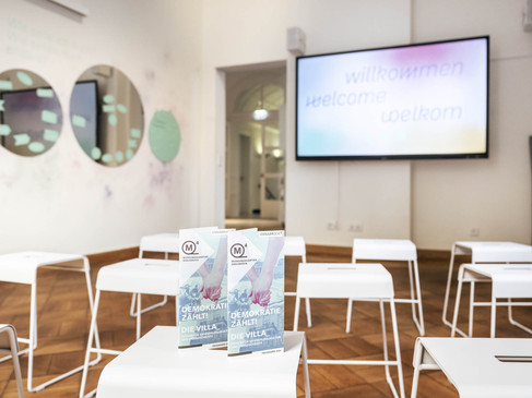 Heller Raum mit weißen Stühlen und Tisch, moderne Wandgestaltung im Museumsquartier, Raum für Events.